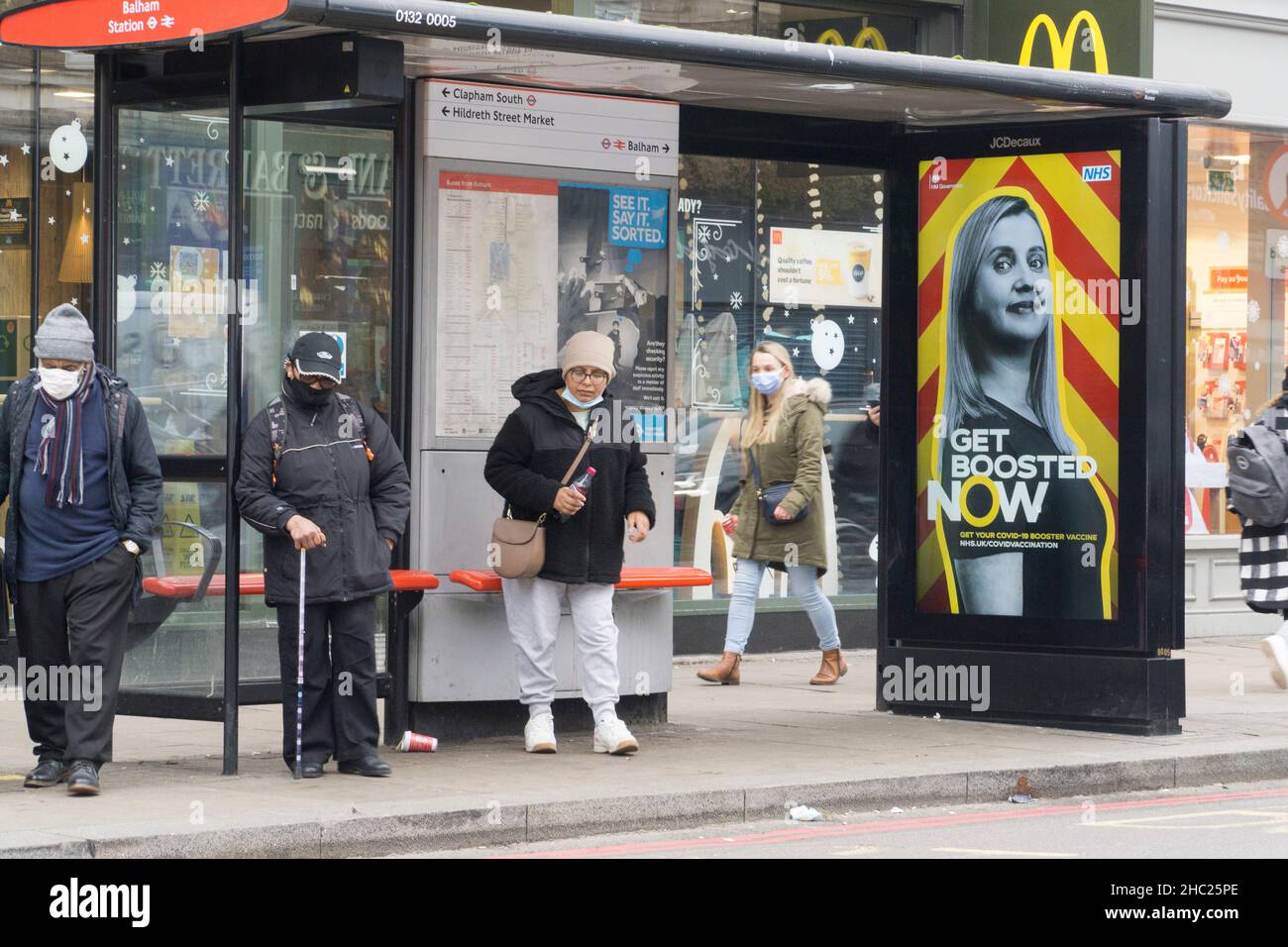 London, Großbritannien, 23. Dezember 2021: An einer Bushaltestelle in Balham stehen Menschen Schlange, die bereits Gesichtsmasken tragen, die jetzt für Fahrgäste im öffentlichen Nahverkehr obligatorisch sind. In den letzten beiden Einkaufstagen vor Weihnachten sind viele Menschen unterwegs, um Lebensmittel und Geschenke zu kaufen. Trotz der sehr hohen Anzahl von omicron-Fällen wurden in England keine neuen Vorschriften eingeführt, die jedoch kurz nach Weihnachten erwartet werden. Anna Watson/Alamy Live News Stockfoto