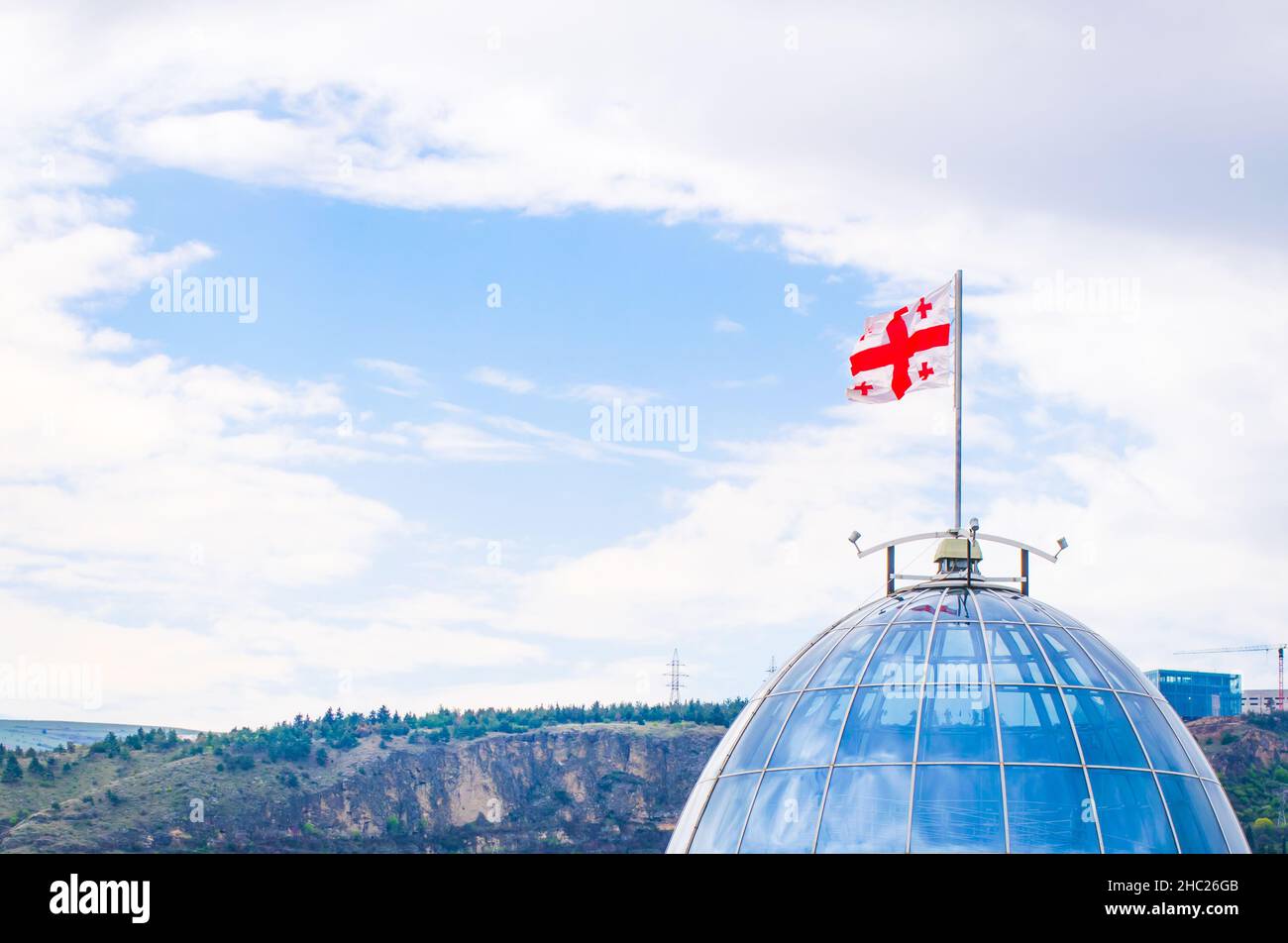 Panoramaansicht des Präsidentenpalastes oben Glaskuppel mit georgischer Flagge, Frühling Natur und Berge im Hintergrund. Konzept der georgischen Politik und Stockfoto