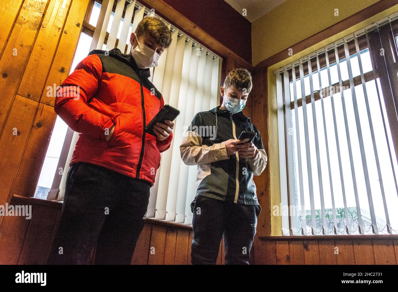 Ardara, County Donegal, Irland. 23rd. Dezember 2021. Junge Menschen schauen sich ihre Smartphones an, während sie warten, bis sie im Ardara Health Center eine Covid19-Coronavirus-Impfstoffinjektion erhalten. Stockfoto