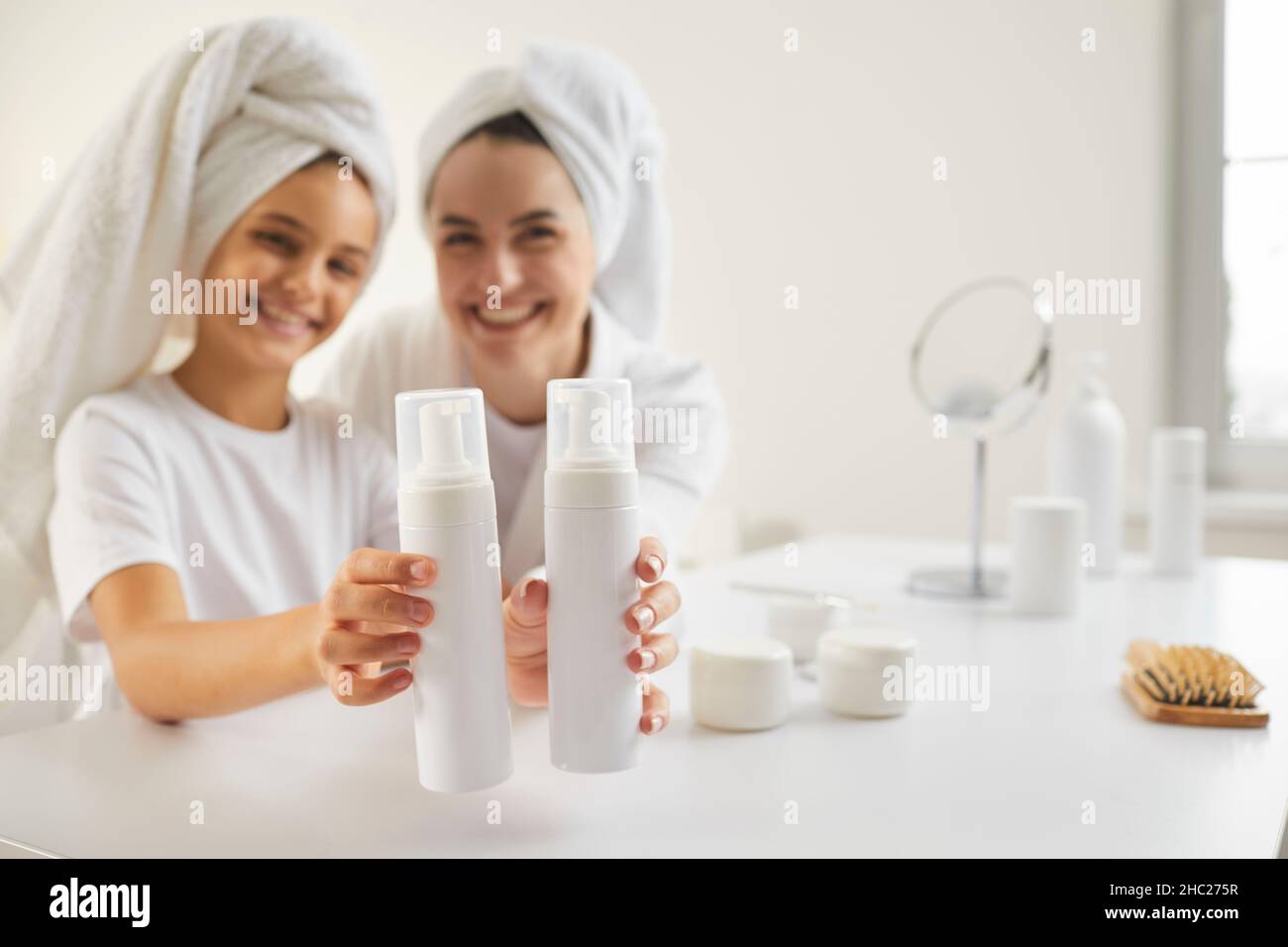 Glückliche Mutter und Kind zeigen zwei Mockup-Flaschen mit Haarpflegeprodukten für die Familie Stockfoto