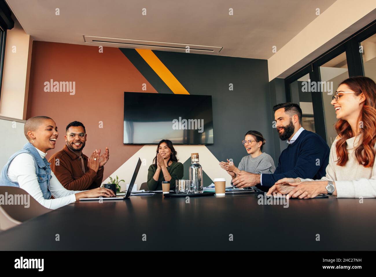 Erfolgreiche Geschäftsleute, die ihren Kollegen in einem Sitzungssaal applaudieren. Eine Gruppe von multiethnischen Geschäftsleuten klatschte während ihrer morgendlichen Briefins fröhlich Stockfoto