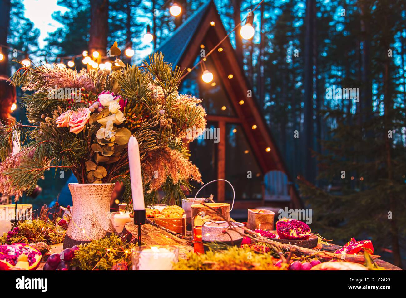 Tischkulisse für eine Hochzeitszeremonie im Öko-Stil im Wald. Dekoration mit frischen Blumen, Kerzen, Moos, Girlanden. Im Hintergrund ist eine blu zu sehen Stockfoto