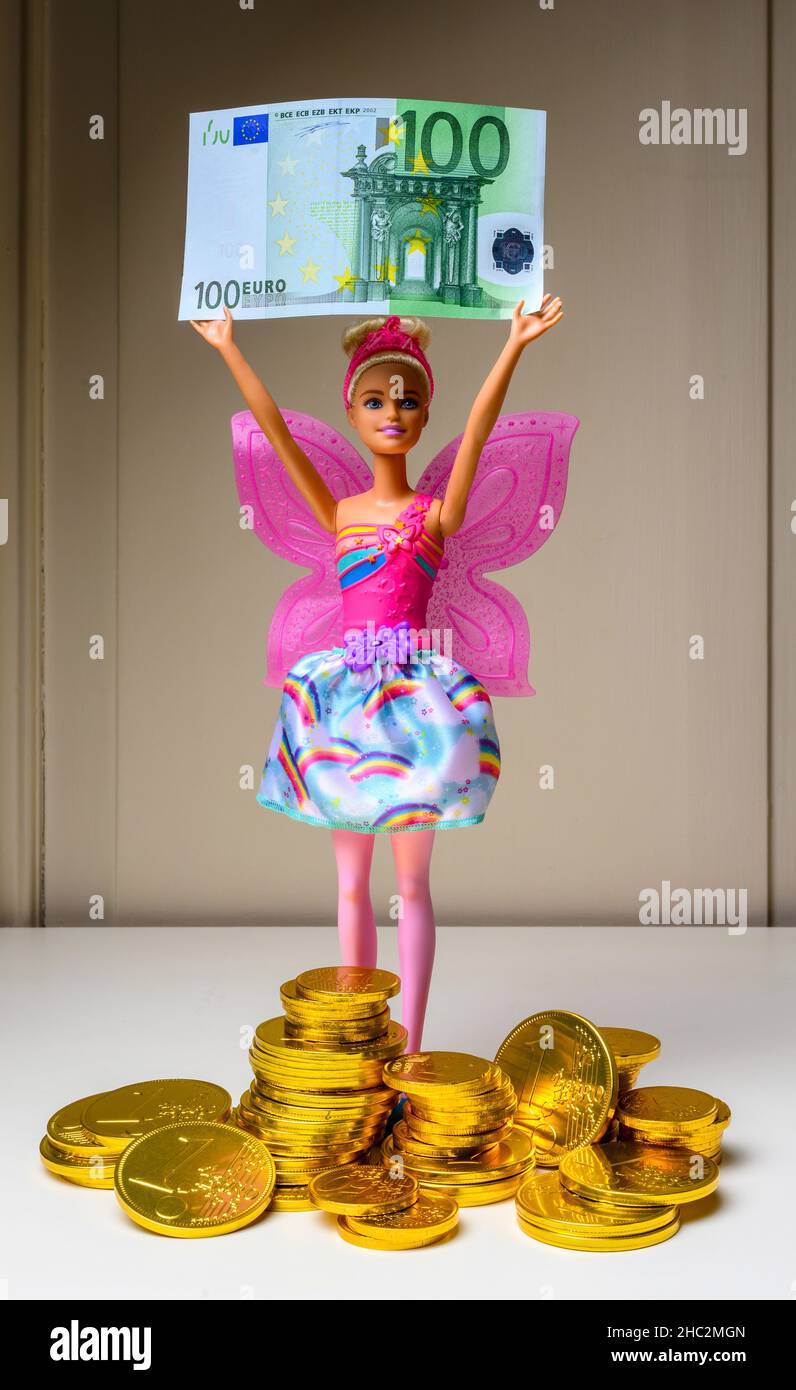 Barbie-Puppe mit einer 100-Euro-Banknote, Stapel Euro-Münzen Pralinen, eingewickelt mit geprägter 1-Euro-Münze aus Goldfolie, Stockfoto