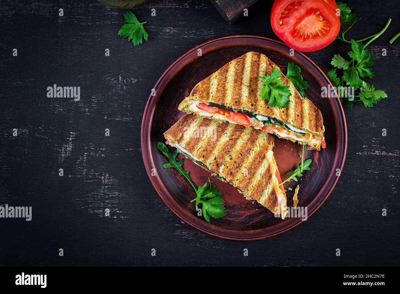 Vegetarische Sandwich Panini mit Spinatblättern, Tomaten und Käse auf einem dunklen Tisch. Toast mit Käse. Draufsicht, Overhead, Kopierbereich Stockfoto