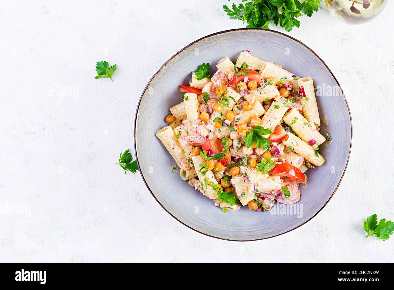 Vegetarische Gemüse-Pasta. Pasta Rigatoni mit Tomaten, roten Zwiebeln, Petersilie und gebratenen Kichererbsen mit Nusssoße. Vegane Küche. Draufsicht, Overhead Stockfoto