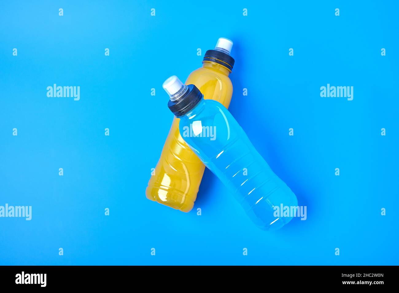 Flaches isotonisches Energy-Orange-Gelb und blaues Sportgetränk in Plastikflaschen auf blauem Hintergrund. Ermöglicht die Aufrechterhaltung des optimalen Wassergleichgewichts Stockfoto
