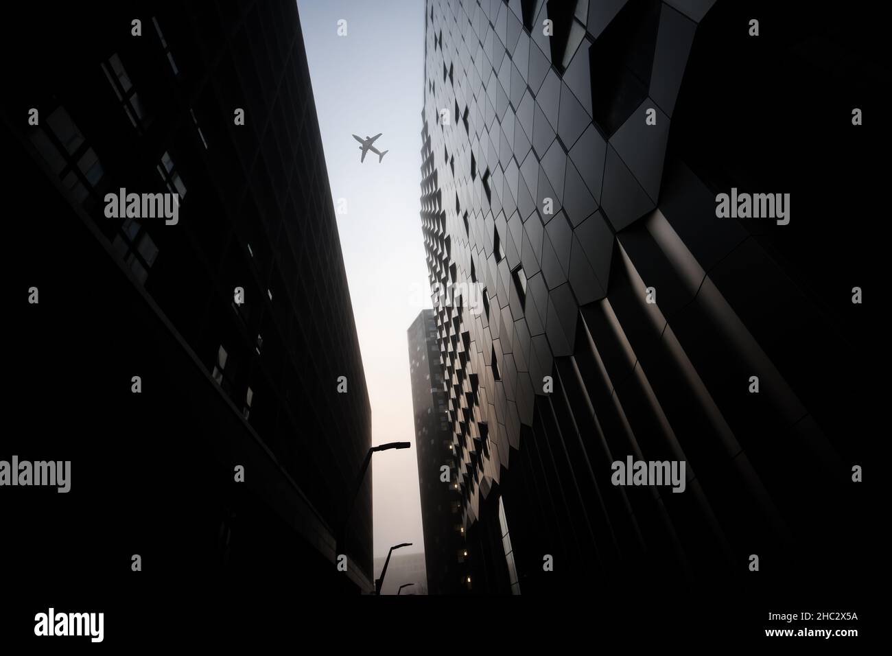 Flugzeug Jumbo Jet Passagierflugzeug fliegen zwischen modernen Stadtzentrum Wolkenkratzer an nebligen nebligen Tag dramatische Beleuchtung und Stahlgebäude futuristisch Stockfoto