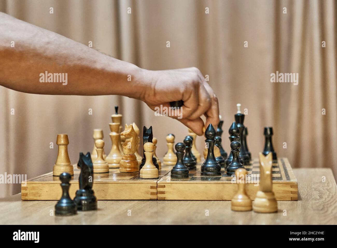 Alte Schachfiguren aus Holz auf Schachbrett. Hand eines erwachsenen Mannes, der sich mit weißem Bauer bewegt Stockfoto