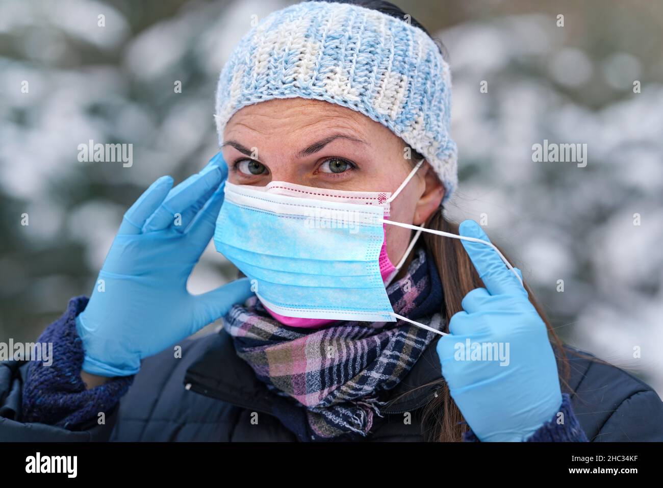 Junge Frau in warmer Winterkleidung trägt rosa Einweg-Virus Gesichtsmaske, setzen eine andere auf - einige raten, dass zwei Schichten bietet bessere Prot Stockfoto