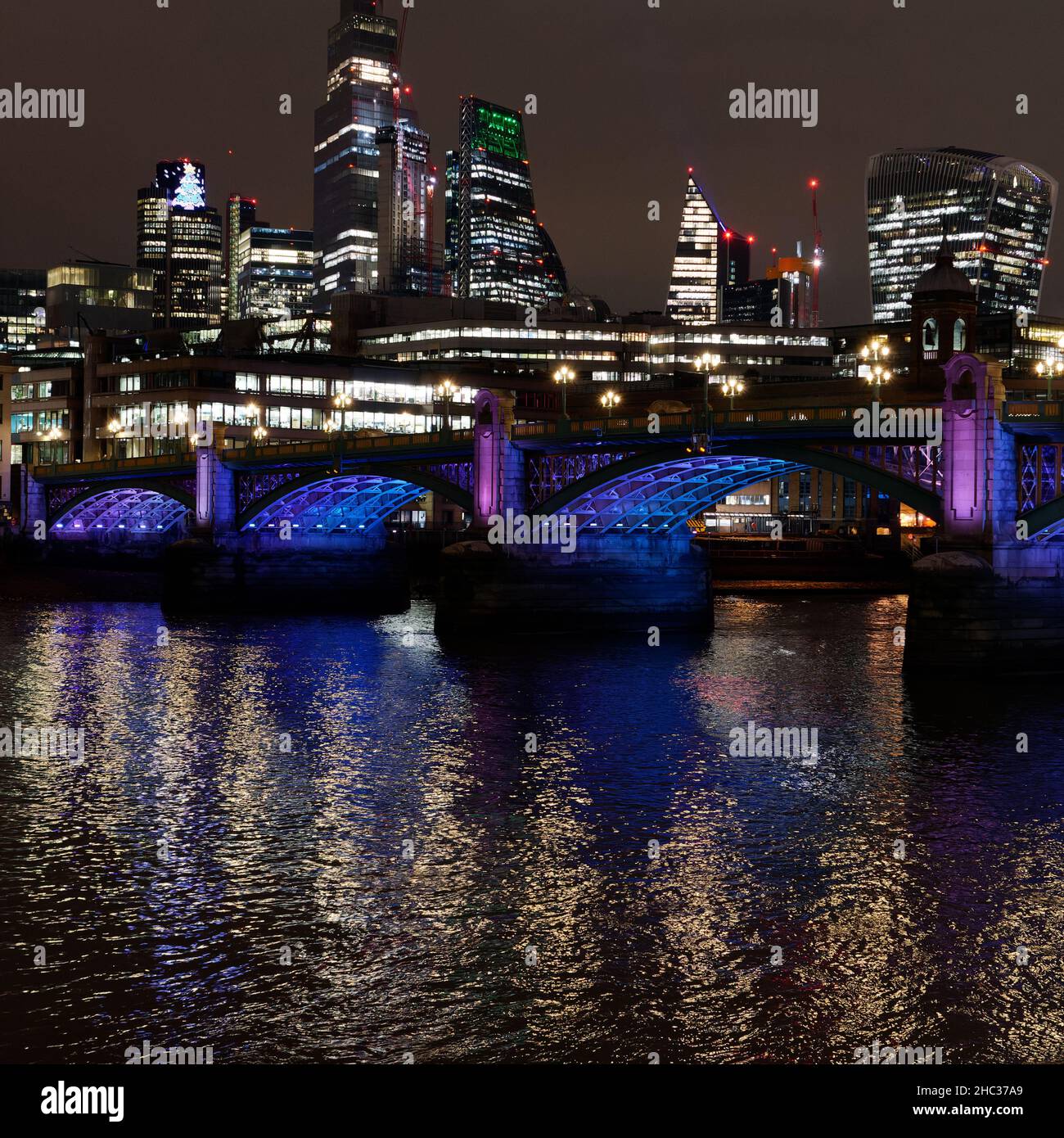Die Lichter der Stadt spiegeln sich in der Nacht im Winter in der Themse mit einer Brücke und Wolkenkratzern im Hintergrund, London. Stockfoto