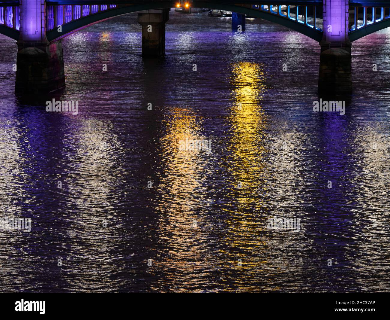 Mehrfarbige Lichter, die in einer Winternacht auf der Themse mit einer Brücke im Hintergrund, London, reflektiert werden. Stockfoto