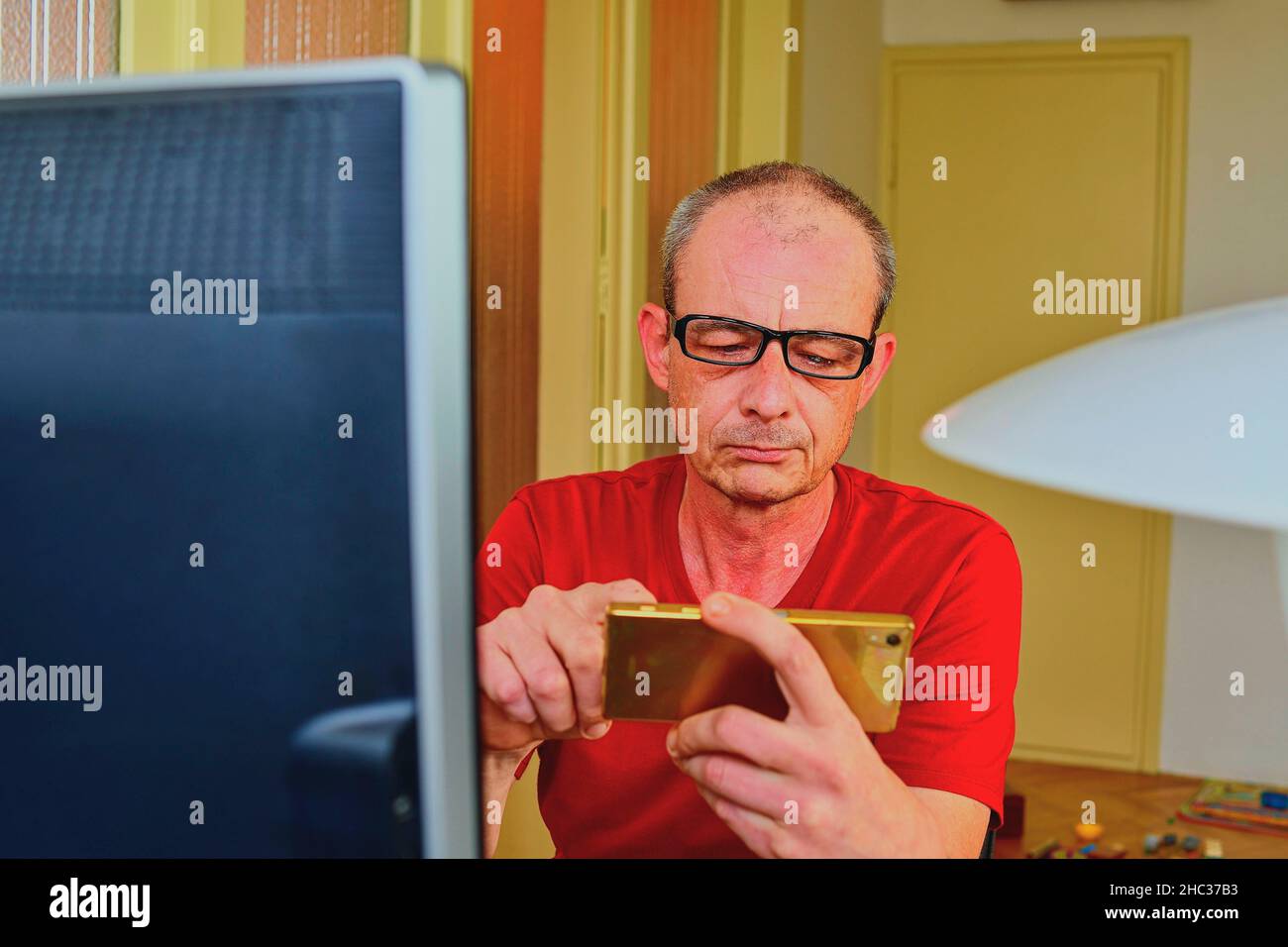 Im mittleren Alter Mann mit Brille am Schreibtisch sitzen. Reifer Mann mit Handy. Senior Concept. Mann an das Home Office Stockfoto Im mittleren Alter Mann mit Brille am Schreibtisch sitzen. Reifer Mann mit Handy. Senior Concept. Mann an das Home Office Stockfoto