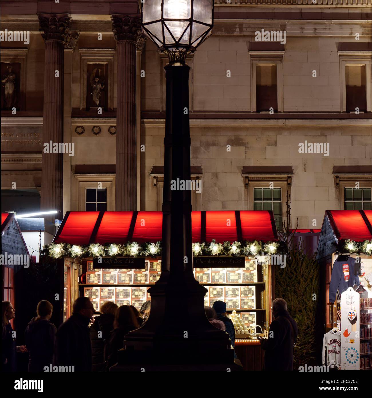 London, Greater London, England, Dezember 15 2021: Besucher eines Weihnachtsmarktes auf dem Trafalgar Square mit einer Straßenlaterne im Vordergrund. Stockfoto
