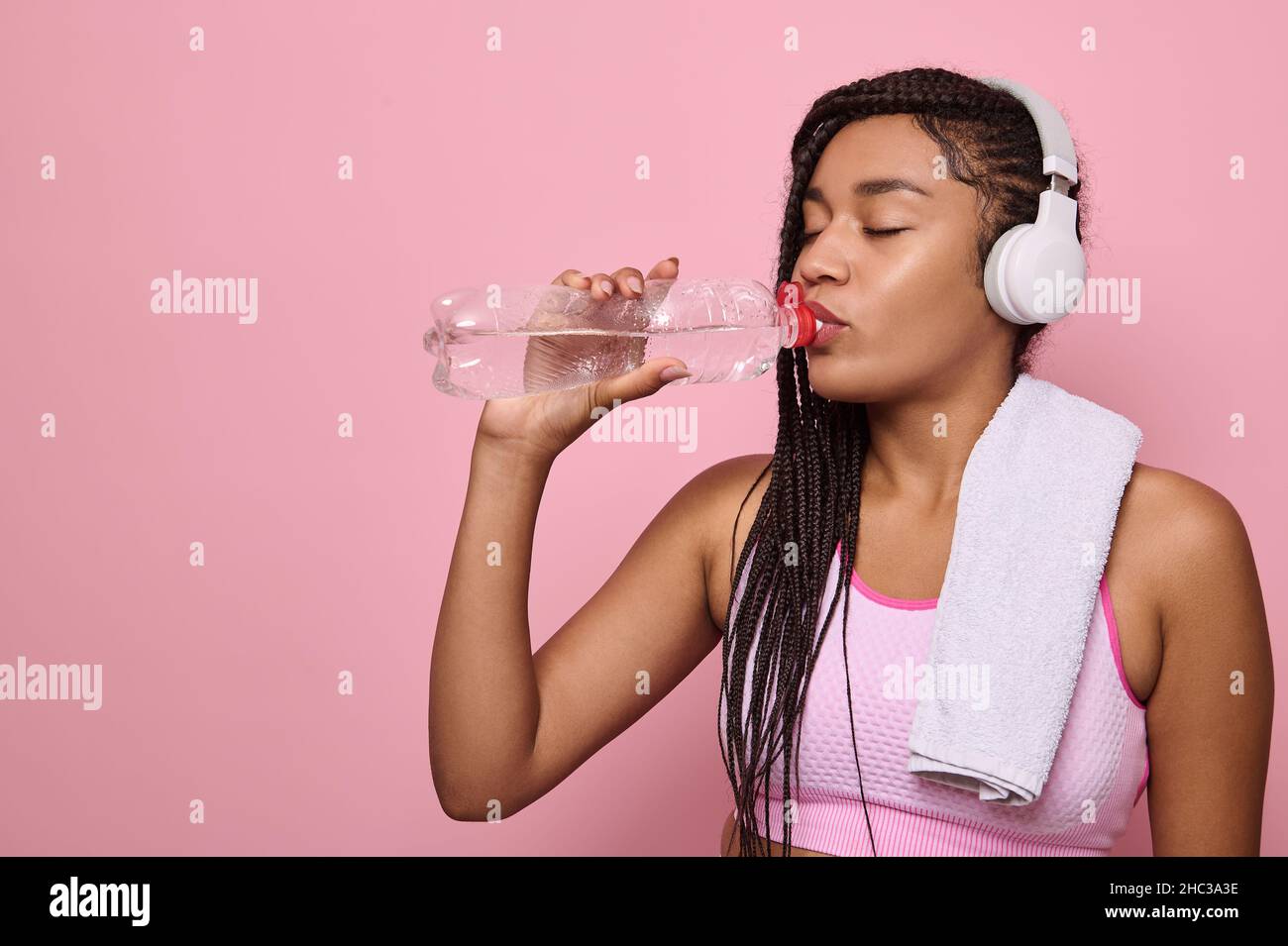 Fitness Frau Trinkwasser steht auf rosa Hintergrund mit Kopierraum. Nahaufnahme einer afrikanischen niedlichen Frau, die nach einem intensiven Training eine Pause einnahm. Mittlere adu Stockfoto