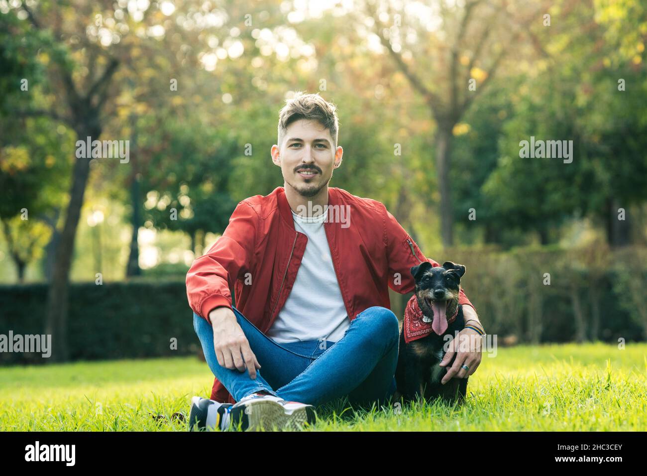 Mann sitzt auf dem Gras neben einem alten Hund mit der Zunge heraus Stockfoto