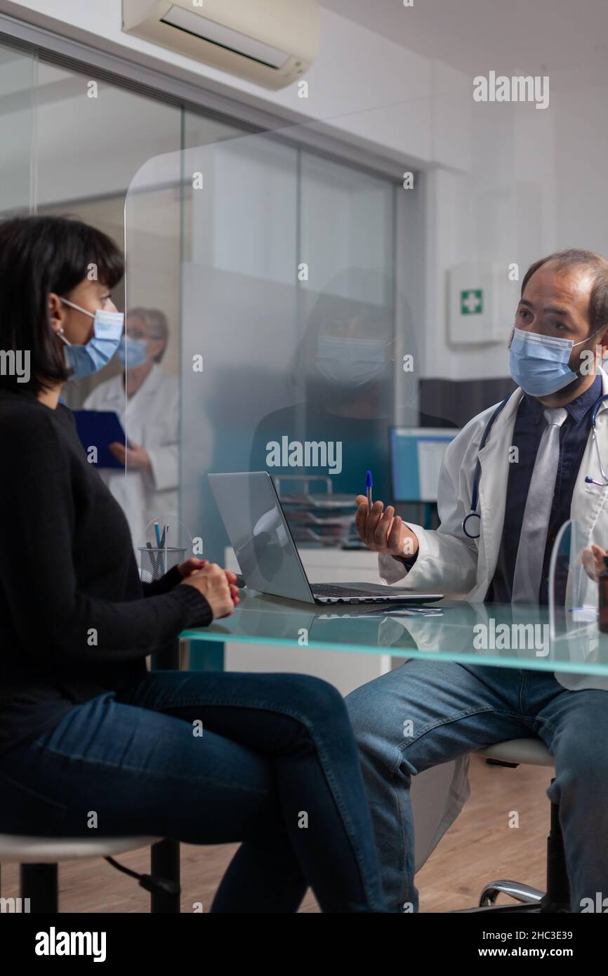 Arzt und Patient diskutieren über die Gesundheitsversorgung bei der Ernennung im Kabinett. Medic spricht mit der Frau über verschreibungspflichtige Medikamente und die Behandlung während einer Coronavirus-Pandemie. Jährliche Kontrollbesichtigung Stockfoto