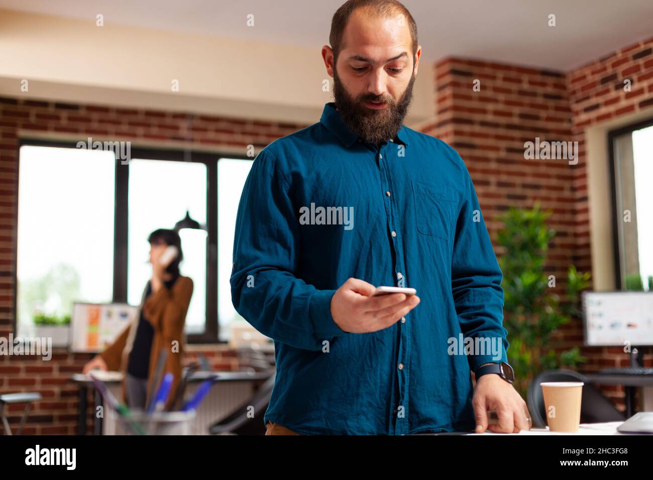 Ein Geschäftsmann, der ein modernes Smartphone hält und auf einen imporanten Anruf wartet, während er bei der Geschäftspräsentation im Büro von Startuo auf die Uhr schaut. Executive Manager analysiert Marketingstrategiepapiere Stockfoto
