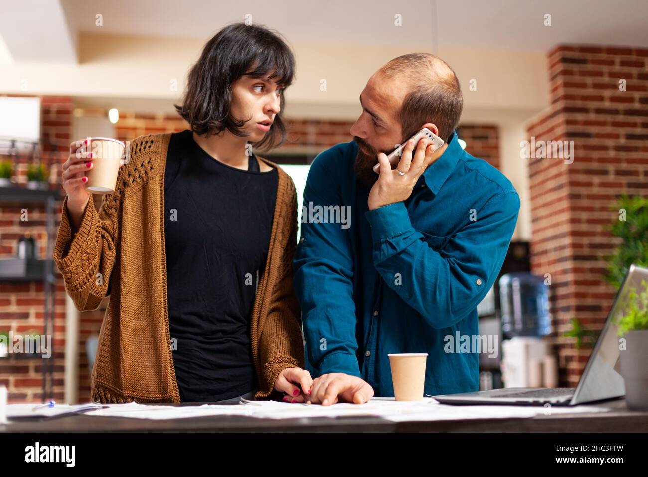 Manager spricht am Telefon mit Geschäftsmann und diskutiert Marketingstrategie, während sie bei der Unternehmenspräsentation mit einer Unternehmerin im Startup Office arbeitet. Geschäftsleute, die Geschäftsdokumente analysieren Stockfoto