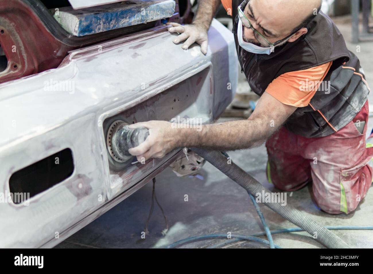 Automechaniker schleift einen Teil eines Autos in einer Garage. Vorbereitung auf die Lackierung des Autos in einer Werkstatt Stockfoto