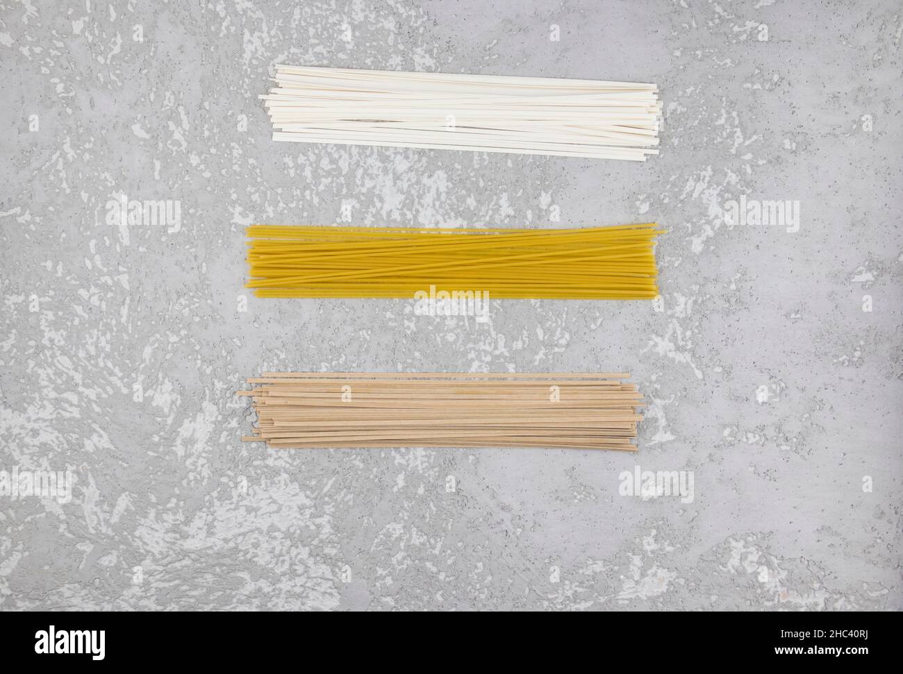 Drei Arten von trockener italienischer Paste auf grauem Betongrund. Nudeln, Spaghetti, Buchweizennudeln. Draufsicht Stockfoto