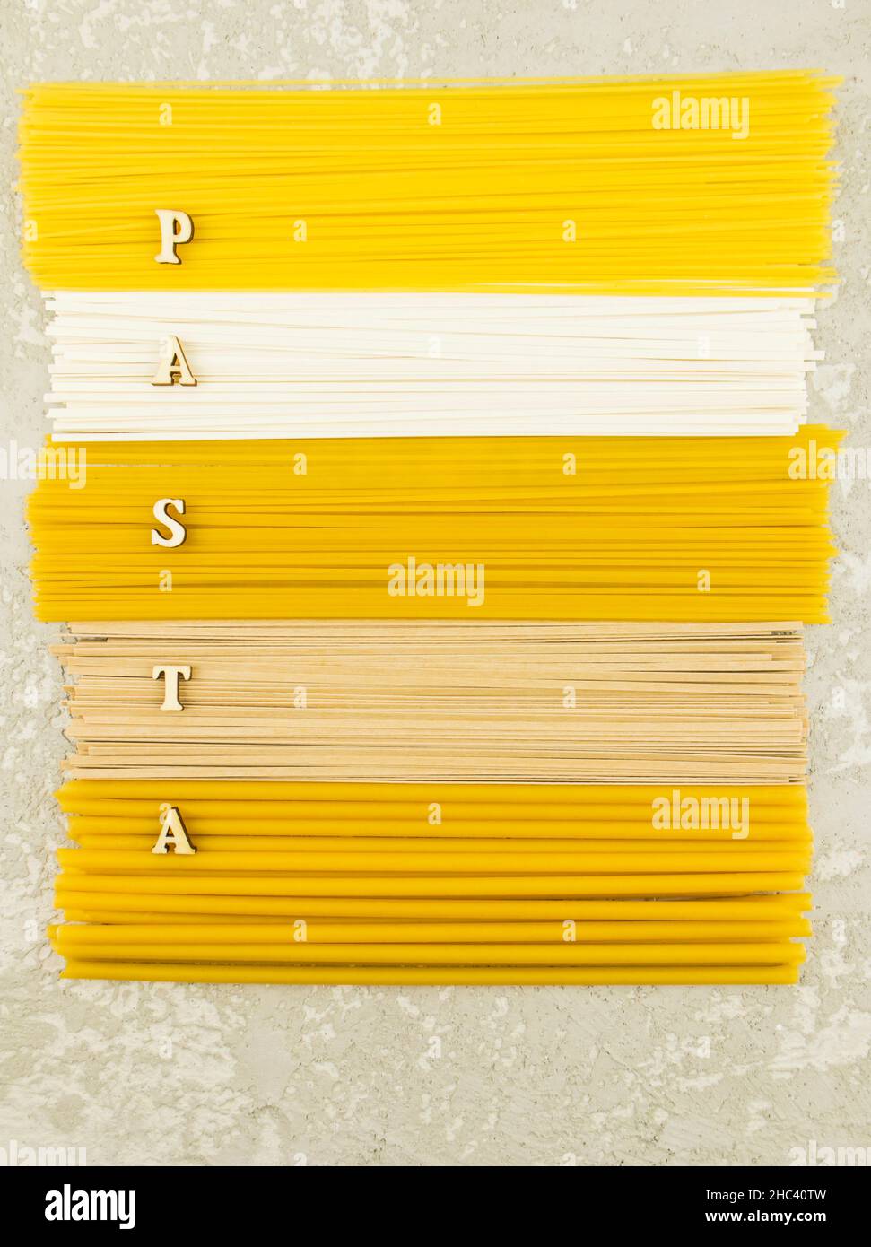 Vertikale flache Ansicht von oben verschiedener italienischer trockener Pasta auf grauem Hintergrund. Holzbuchstaben mit dem Wort -Pasta Stockfoto