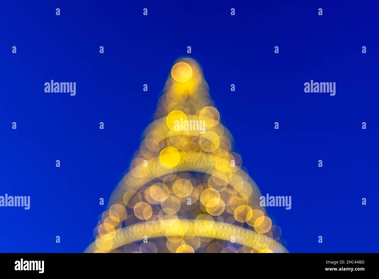 Verschwommenes Bokeh von Weihnachtsbaum mit Lichterketten auf blauem Hintergrund. Stockfoto
