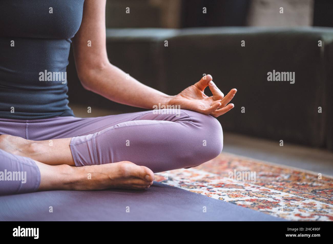 Frau, die in Lotus-Pose sitzt und mit offenen Händen meditiert. Yoga-Frau praktiziert Yoga-Meditationsübung auf der Matte in ihrem Wohnzimmer zu Hause. Nahaufnahme. Hochwertige Fotos Stockfoto