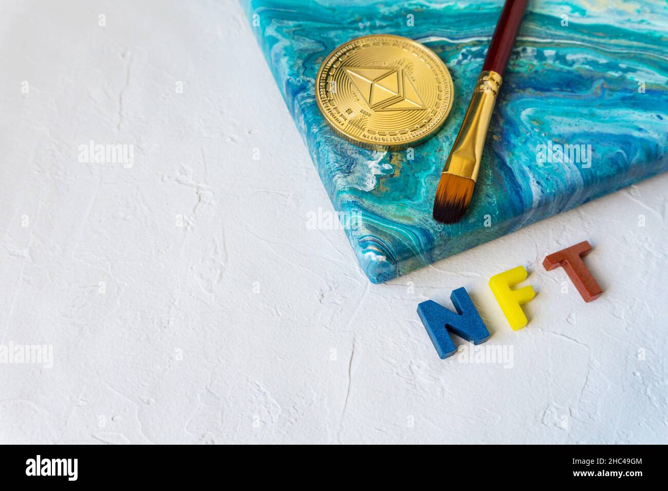 Nicht-fungible Token-Konzept. NFT Wort neben Ethereum Krypto Münze und Pinsel auf Leinwand mit Malerei auf weißem Hintergrund mit Kopierraum für Text. Stockfoto