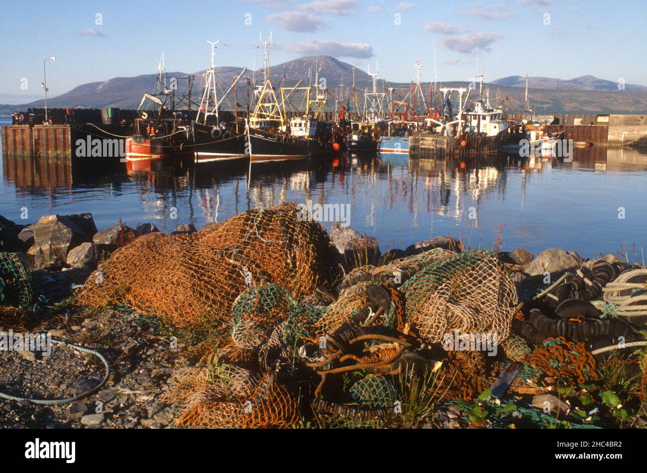 Trawler, die am Kai festgemacht haben, spiegeln sich im Hafen von Carradale Bay mit leeren Netzen am Kai Mull von Kintyre Schottland wider Stockfoto
