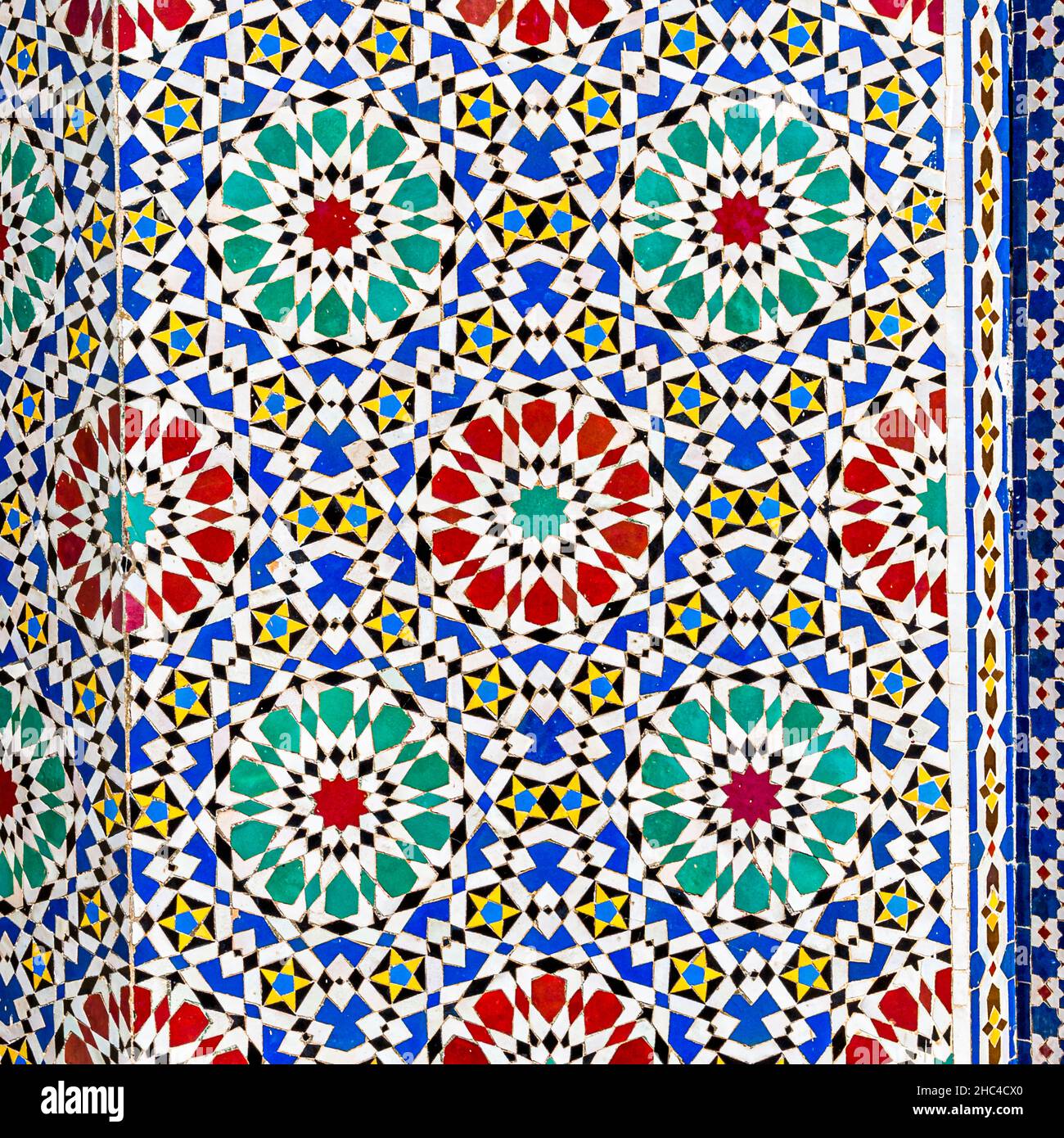 Ein Sternmuster aus roten, türkisfarbenen und blauen Zellige-Fliesen bedeckt die Wand im Königspalast in Fès, Marokko. Stockfoto