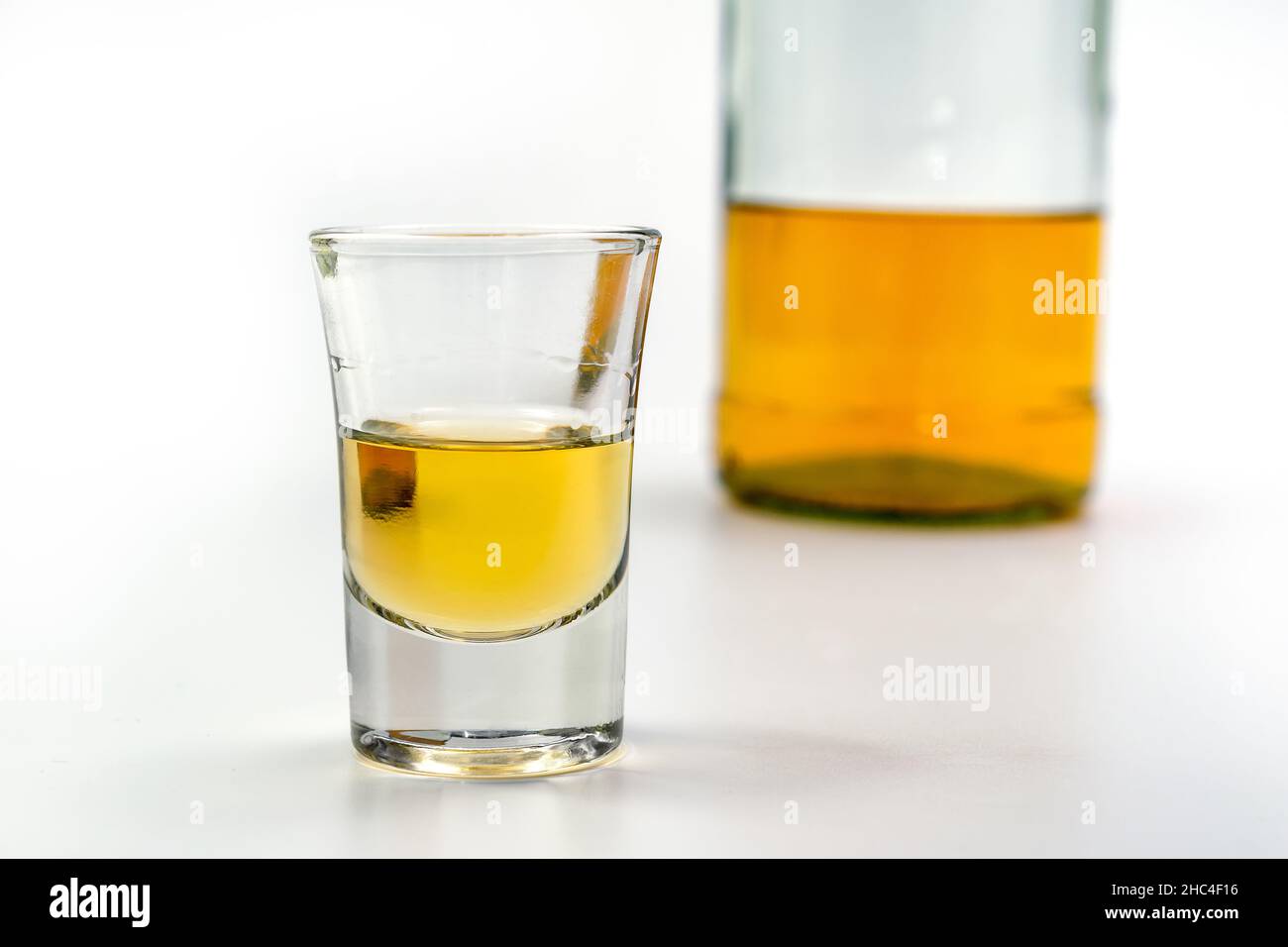 Alkoholisches Getränk in einem Glas und eine Flasche Brandy auf der Rückseite auf dem weißen Tisch. Starker Alkoholvergiftung. Das Konzept der Alkoholabhängigkeit. Alcoh Stockfoto