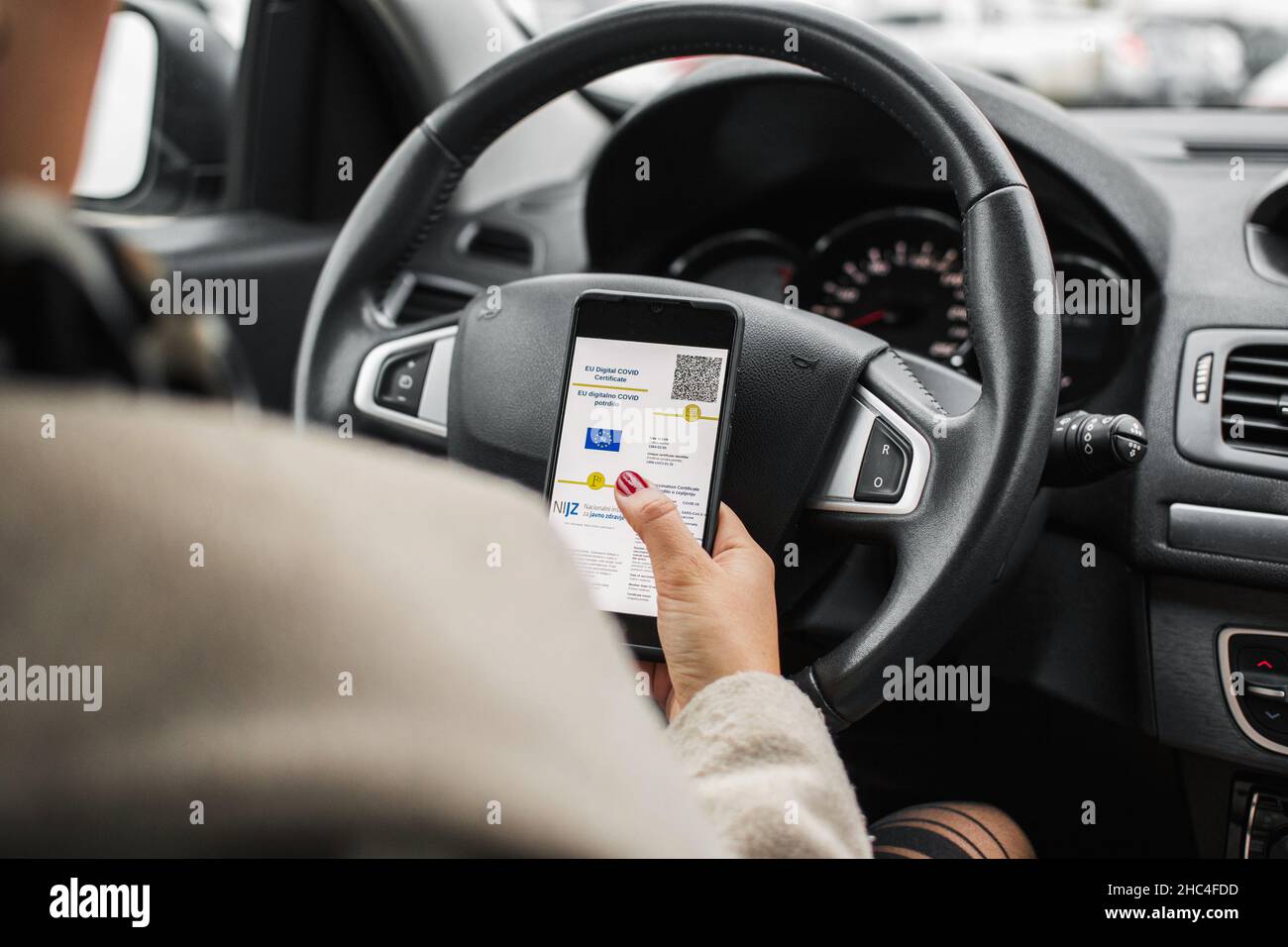 Fahrer sitzt im Auto, hält Mobiltelefon mit digitalem Covid-Pass oder Impfpass Stockfoto