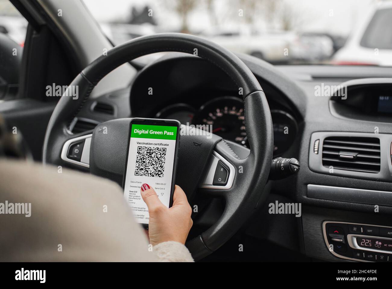 Fahrer sitzt im Auto, hält Mobiltelefon mit digitalem Covid-Pass oder Impfpass Stockfoto