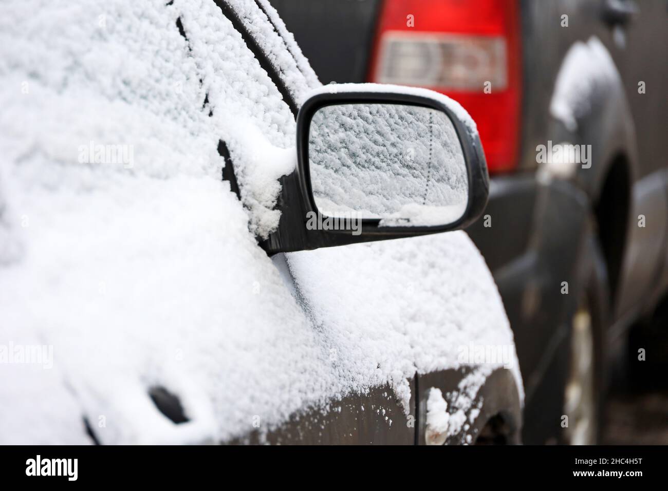 Auto mit Schnee bedeckt, Rückspiegel bei frostigen Wetter. Transport auf dem Parkplatz nach Schneefall im Winter Stockfoto