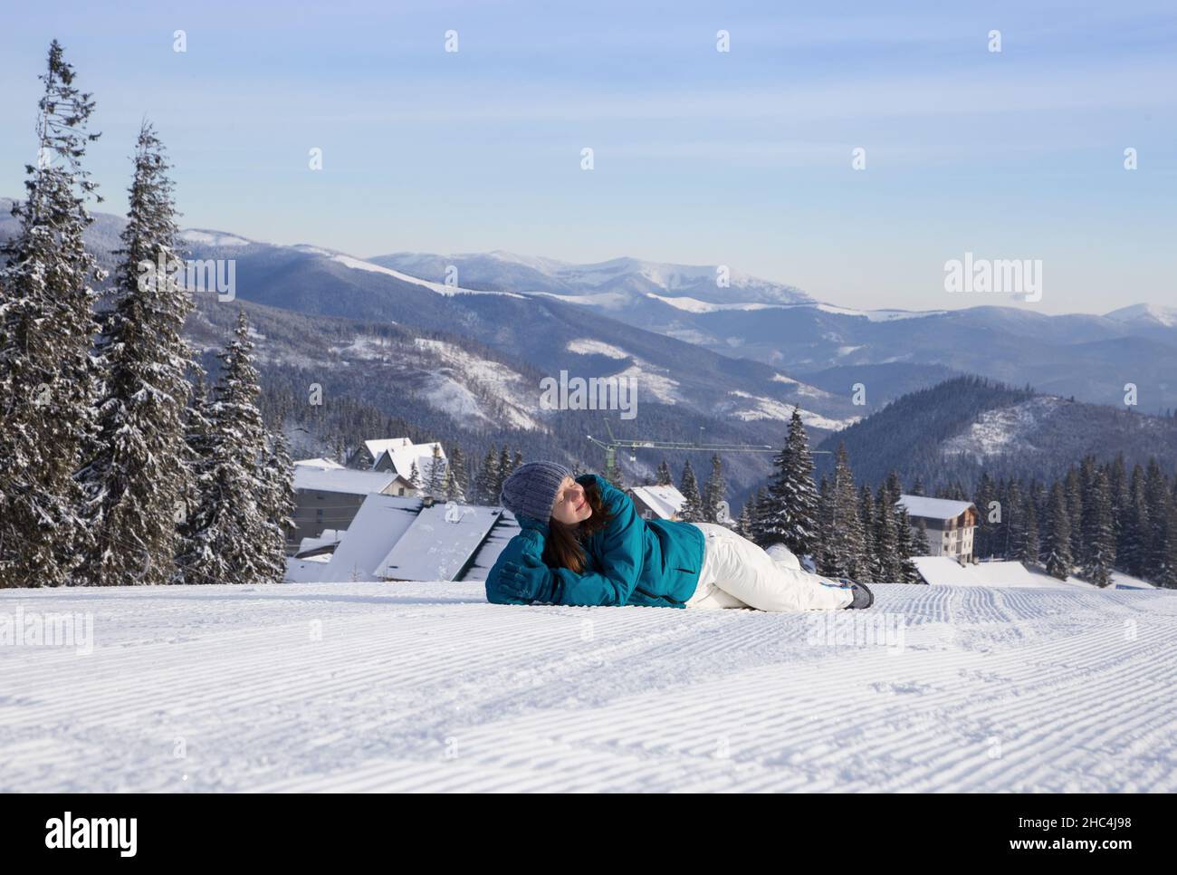 Frau in guter Laune liegt im Schnee vor dem Hintergrund einer Landschaft von schneebedeckten Bergen. Kalten Winter sonnigen Tag. Winterurlaub, Spaziergänge o Stockfoto