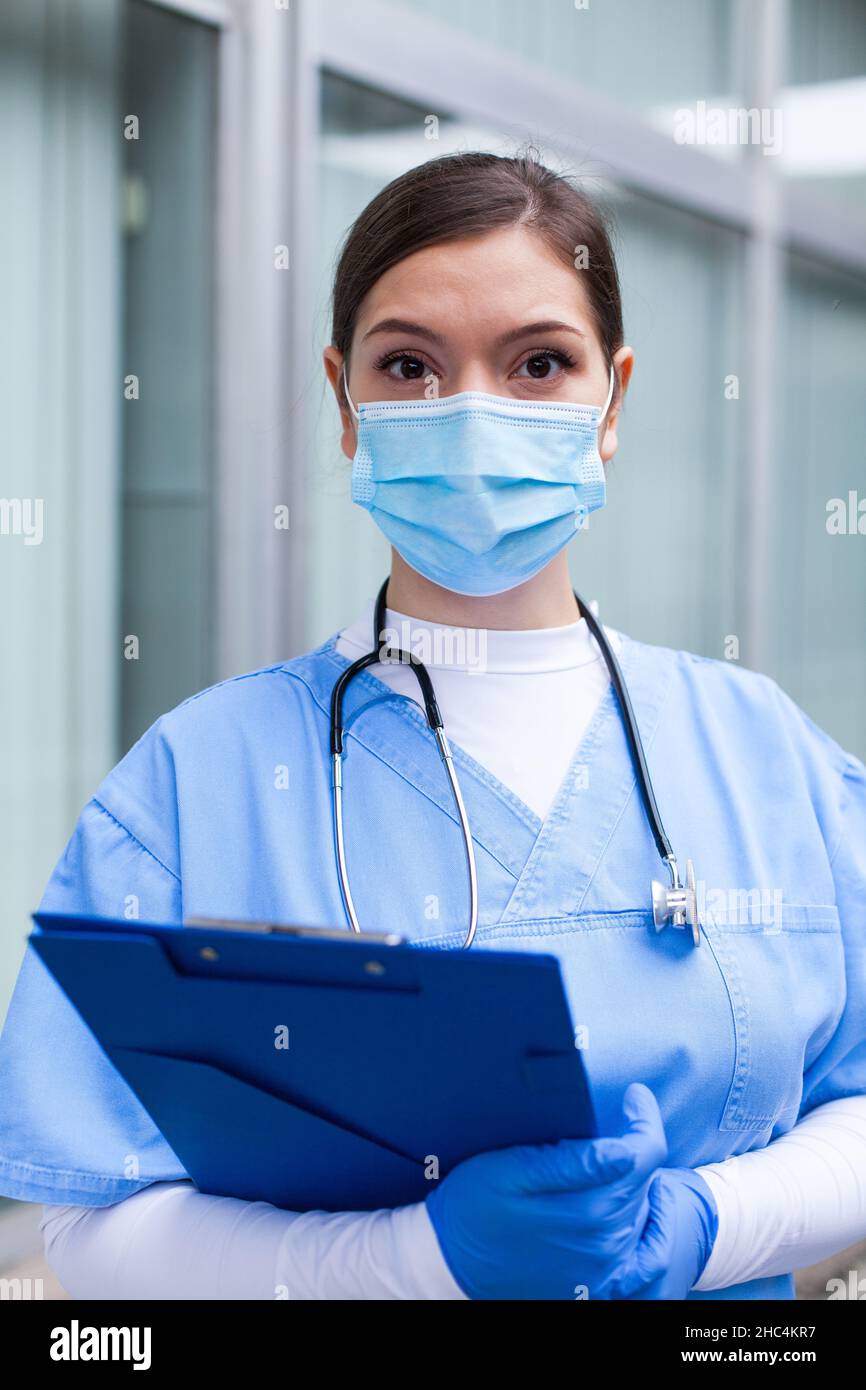 Nahaufnahme Porträt von der Taille nach oben einer Frau Arzt, junge NHS UK weibliche kaukasischen medizinischen Spezialisten trägt schützende chirurgische Gesichtsmaske, Handschuhe, ste Stockfoto