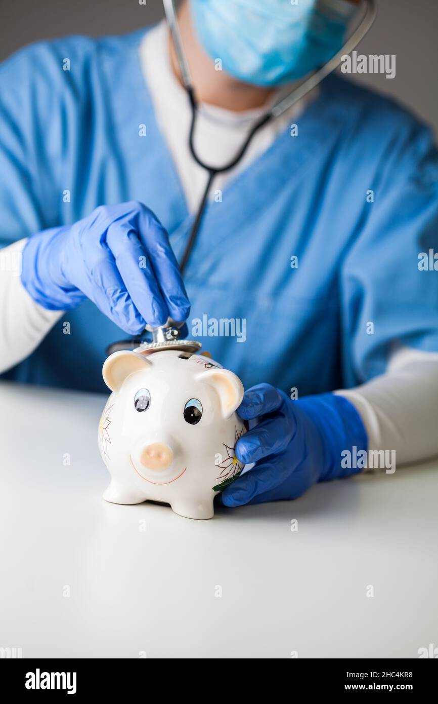 Arzt hört dem Sparschwein-Puls mit Stethoskop zu, konzeptuelle Darstellung von Wirtschaftscrashs, monetärer Kollaps durch COVID-19 Coronavirus-PAN Stockfoto