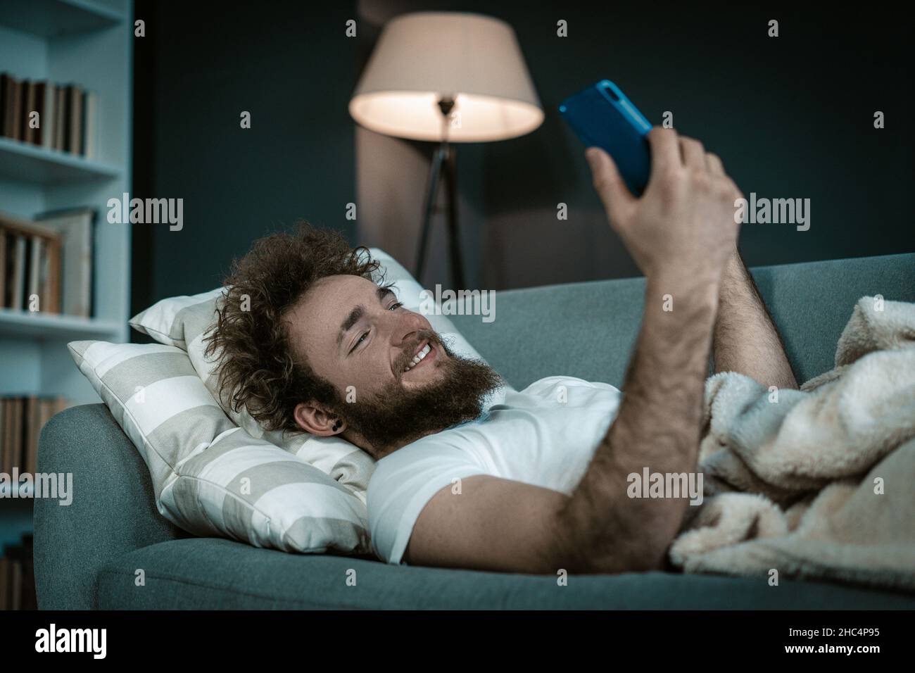 Wohlgeformter Kerl beobachtet seine Lieblingsserien auf seinem Handy, bevor er einschläft. Er beobachtet die ganze Nacht in seinem Bett Serienartikel. Nahaufnahme. Hochwertige Fotos Stockfoto