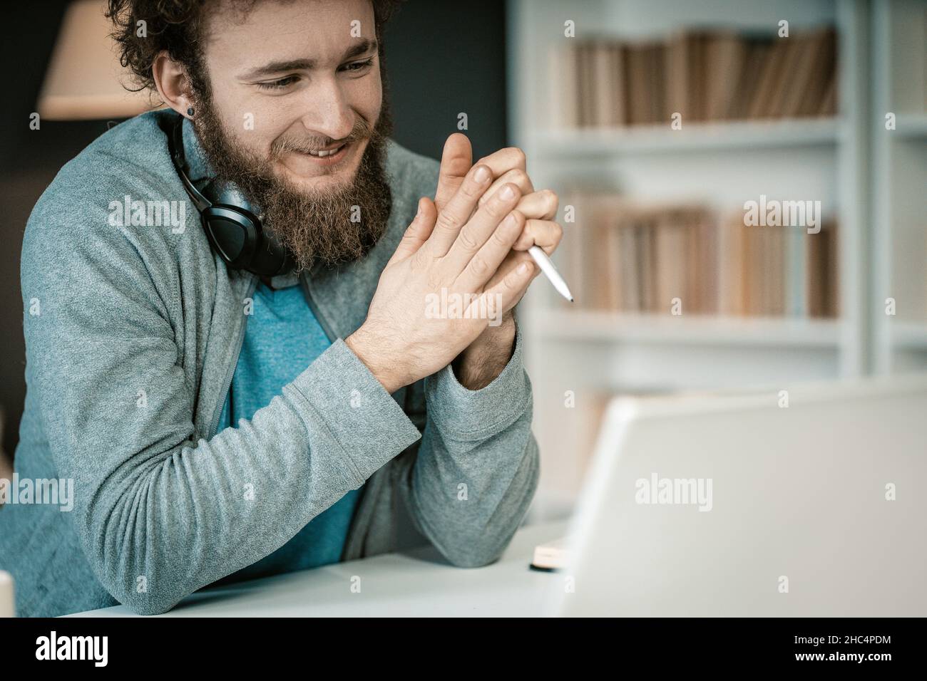 Shy Student hat eine Online-Videostunde mit seinem Laptop in seiner Heimatbibliothek. Während der Quarantäne hat der Student Fernunterricht. Regale voller Bücher Hintergrund. Nahaufnahme. Hochwertige Fotos Stockfoto