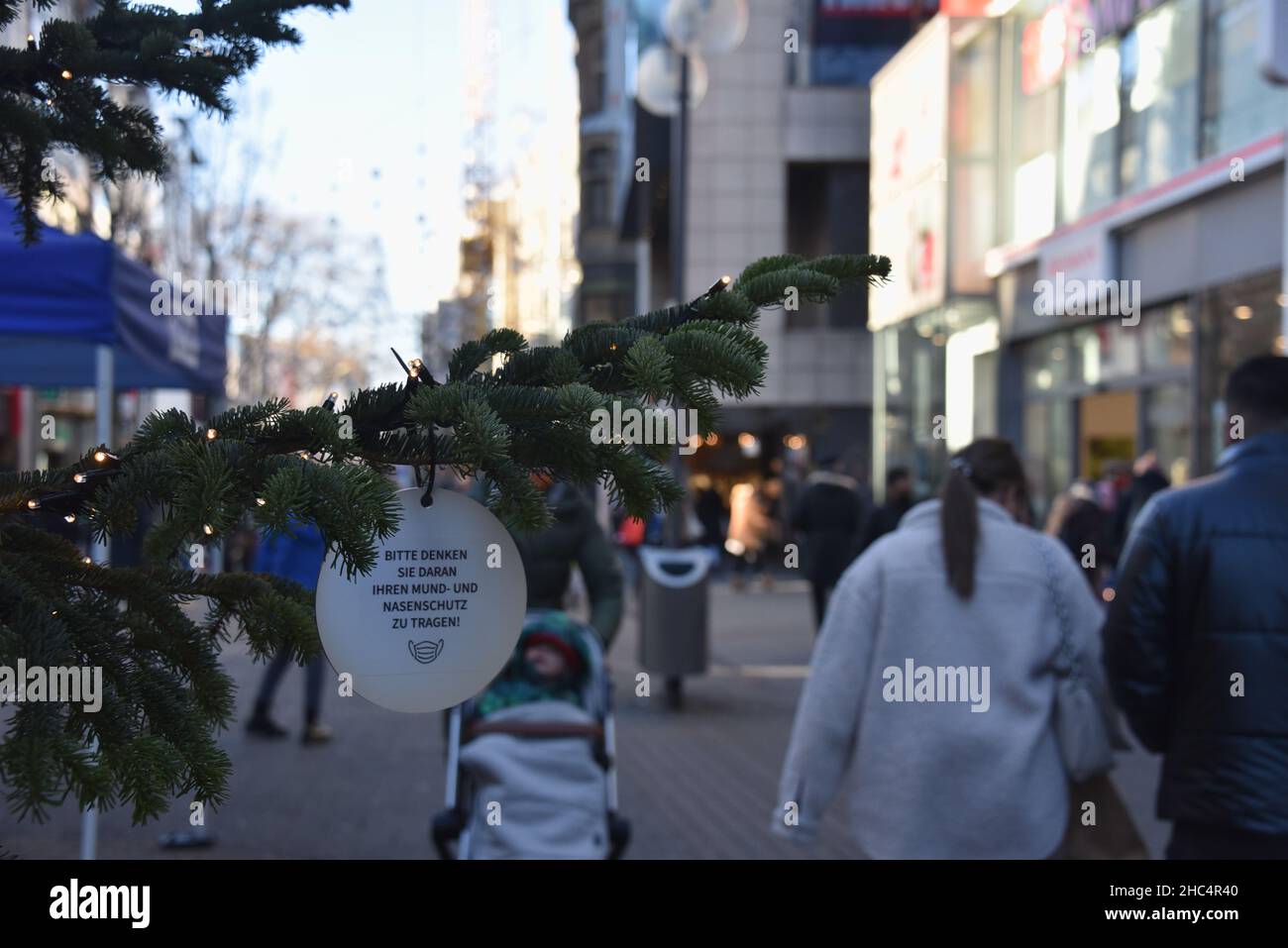 Köln, Deutschland. 21st Dez 2021. Eine Weihnachtskugel auf einem beleuchteten Tannenzweig mit der Aufschrift bitte denken Sie daran, eine Maske, Mund- und Nasenschutz in der Kölner Fußgängerzone zu tragen. Quelle: Horst Galuschka/dpa/Alamy Live News Stockfoto