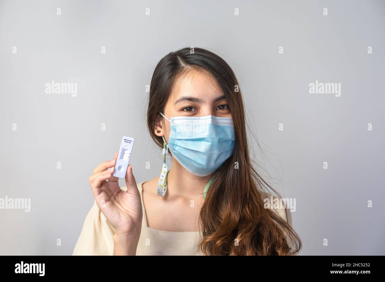 Asiatische Frau mit Gesichtsmaske, die ein negatives Ergebnis eines schnellen Antigentestkits bei Hausgebrauch zeigt. Keine Infektion mit Covid-19, Coronavirus Stockfoto