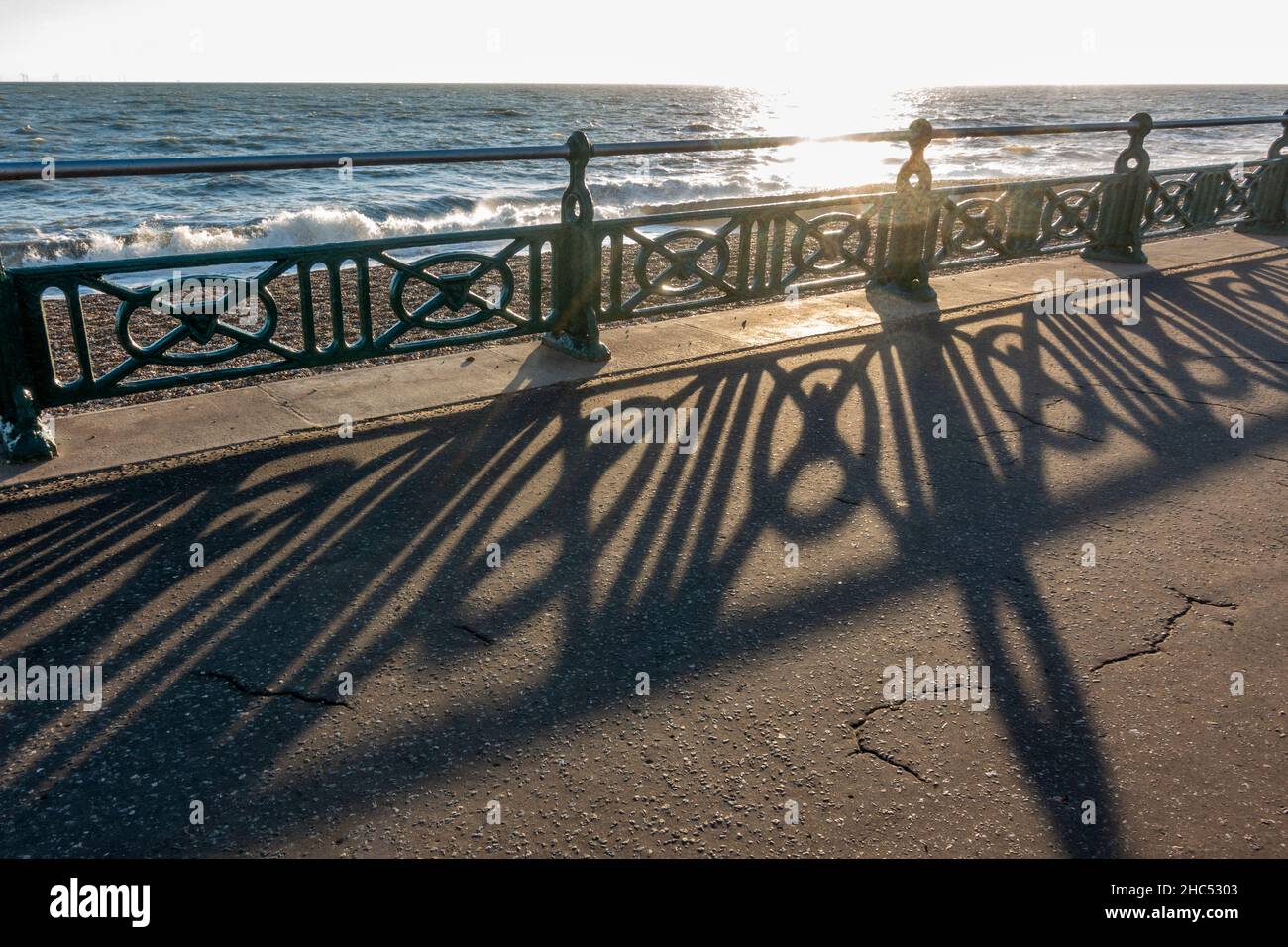 Untergehende Sonne scheint durch die Geländer entlang der Küste am Brighton Beach, Brighton, East Sussex, Großbritannien. Stockfoto