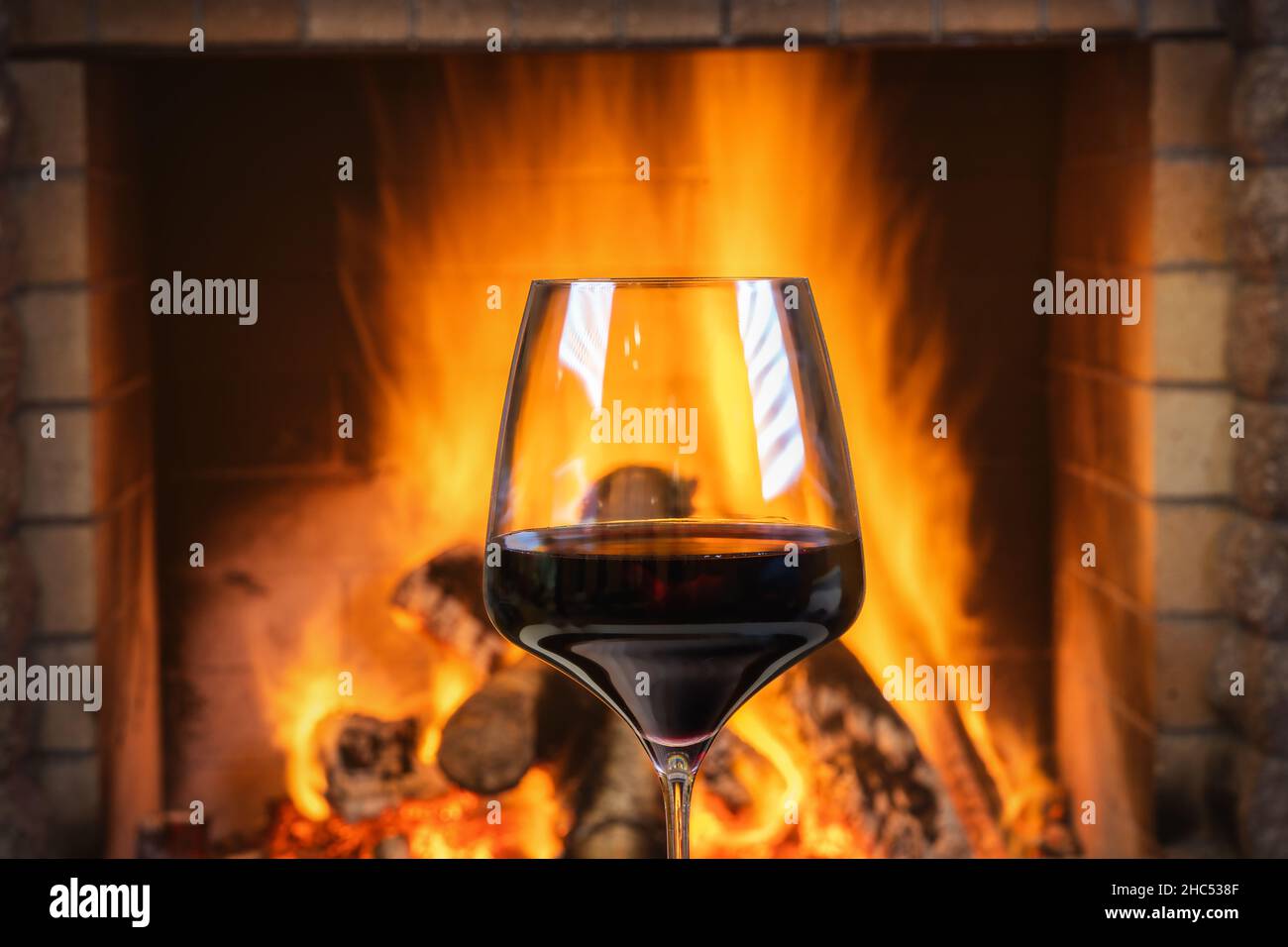 Ein Glas Rotwein in der Nähe eines gemütlichen Kamins, . Stockfoto