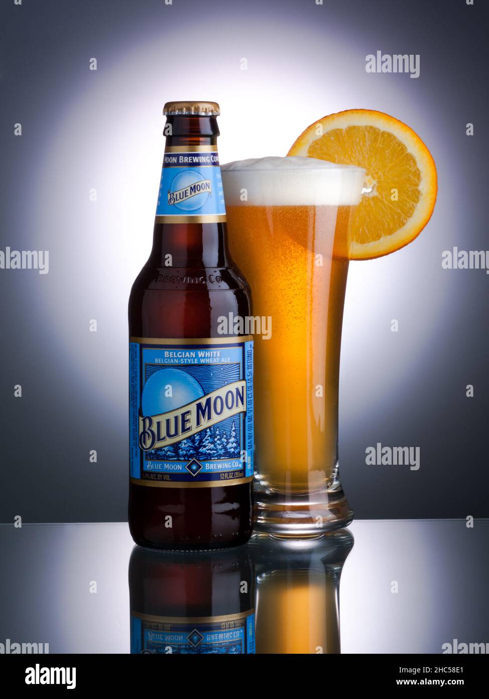 Vertikale Nahaufnahme der Blue Moon Bierflasche und ein volles Glas Bier auf einer reflektierenden Oberfläche. Stockfoto