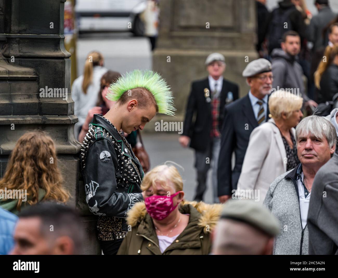 Ein junger Mann, der sein Telefon mit einer mohikanischen Punk-Frisur unter einer Menschenmenge anschaut, Royal Mile, Edinburgh, Schottland, Großbritannien Stockfoto