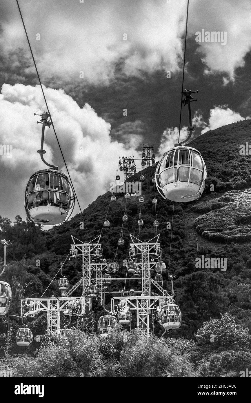 Szenische Schwarz-Weiß-Aufnahme einer Seilbahn, die über den Wald zu den Hügeln hinauffährt Stockfoto