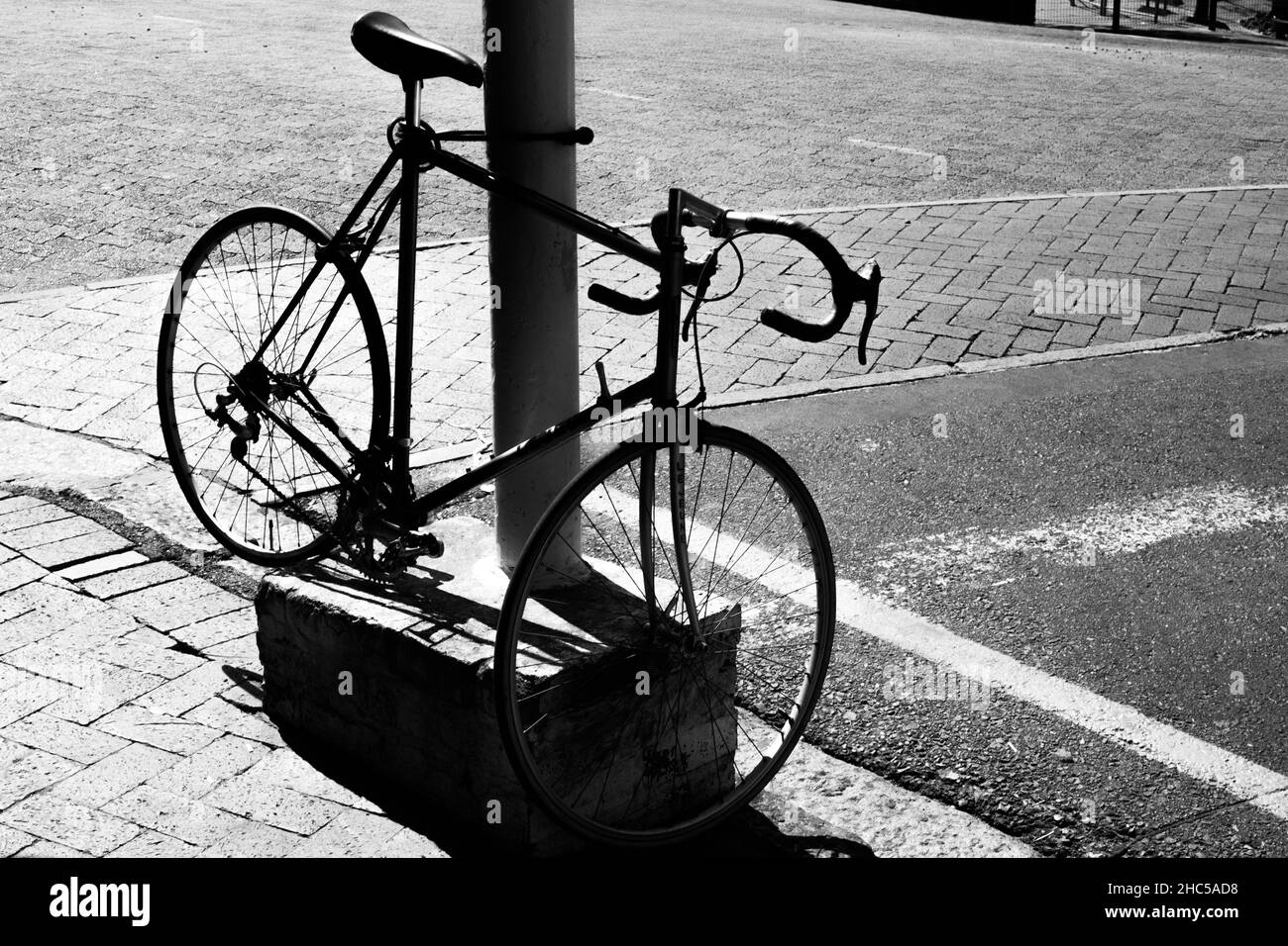 Szenische Schwarz-Weiß-Aufnahme eines Fahrrads, das in der Nähe der Straße geparkt ist Stockfoto