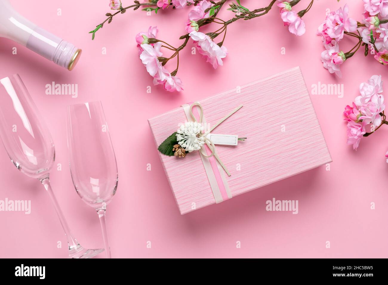 Frühlingsblumen, Gläser, Champagner und Geschenkbox auf festlichem rosa Hintergrund. Romantische Grußkarte zum Valentinstag. Internationaler Frauentag, ce Stockfoto