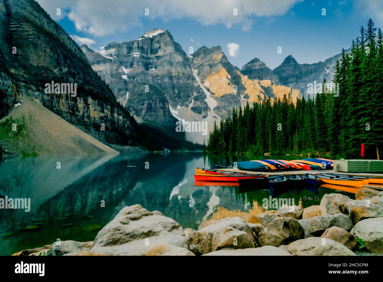 Ruhiger See mit Pier und bunten Booten, umgeben von Bergen und Bäumen im Banff National Park Stockfoto