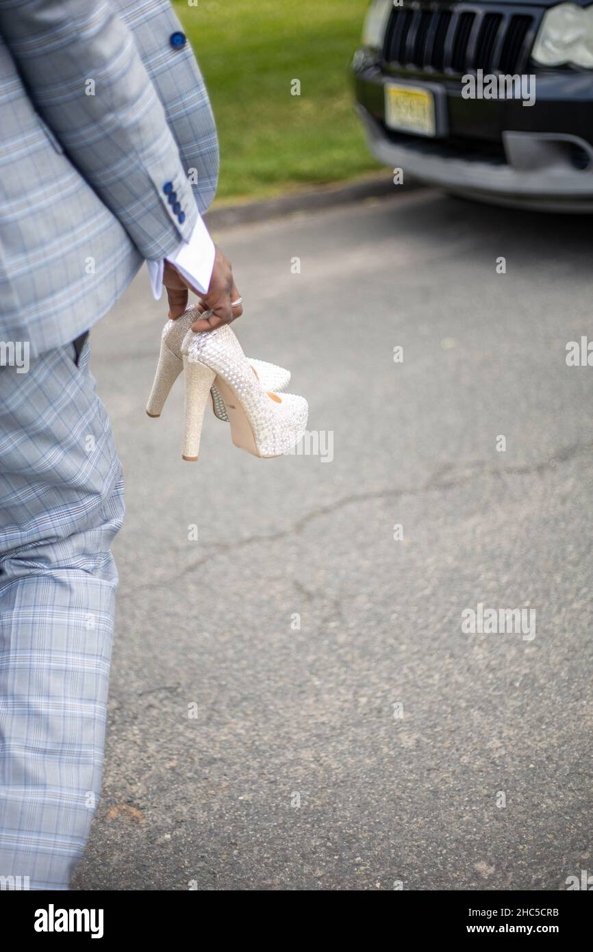 Vertikale Aufnahme eines Bräutigams, der auf der Autobahn läuft und in der Hand weiße Schuhe der Braut hält Stockfoto